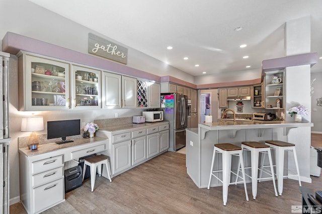 kitchen with white microwave, light wood-style flooring, freestanding refrigerator, a kitchen bar, and a sink