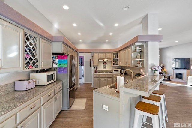 kitchen featuring appliances with stainless steel finishes, open shelves, wood finished floors, and a kitchen breakfast bar