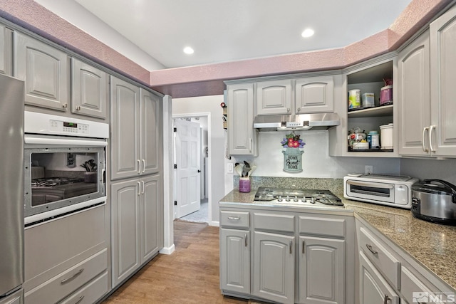 kitchen with white oven, gray cabinets, stainless steel gas stovetop, and under cabinet range hood