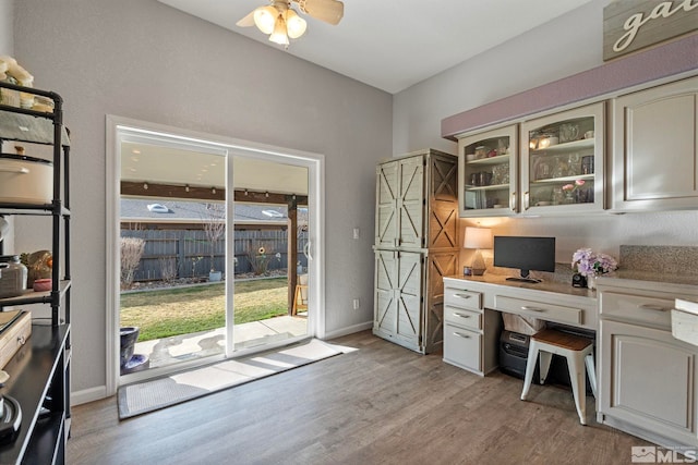 office space featuring light wood-style floors, built in study area, ceiling fan, and baseboards