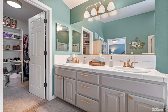 full bath with backsplash, a sink, a spacious closet, and double vanity