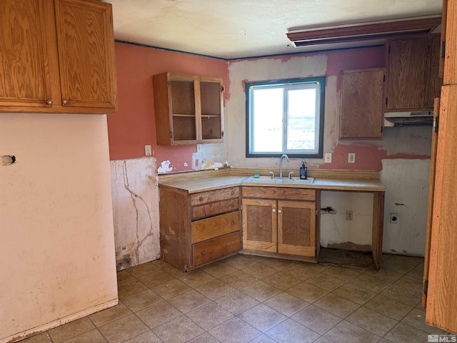 kitchen featuring brown cabinets, light countertops, under cabinet range hood, open shelves, and a sink