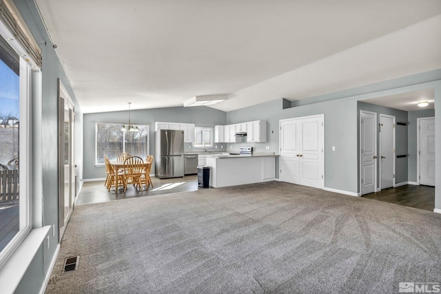 unfurnished living room with lofted ceiling, an inviting chandelier, visible vents, and dark colored carpet