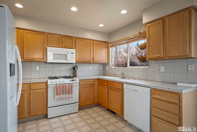 kitchen featuring white appliances, light floors, recessed lighting, a sink, and tile counters