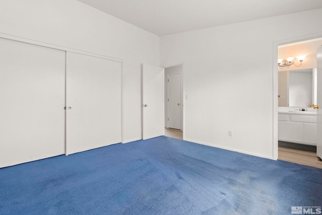 unfurnished bedroom featuring a closet, light colored carpet, ensuite bathroom, and a sink