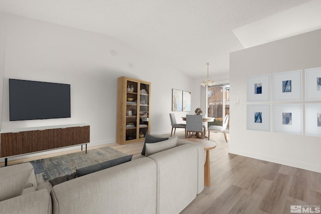 living area with vaulted ceiling, a notable chandelier, baseboards, and light wood finished floors