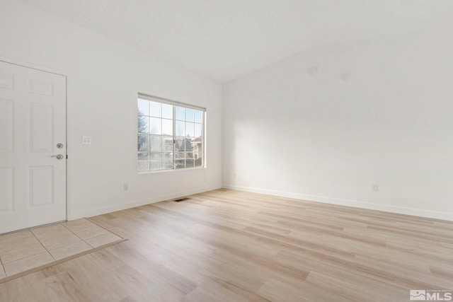 unfurnished room with vaulted ceiling, visible vents, baseboards, and light wood finished floors