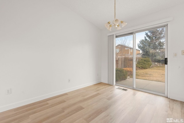 unfurnished dining area with visible vents, a notable chandelier, wood finished floors, baseboards, and vaulted ceiling