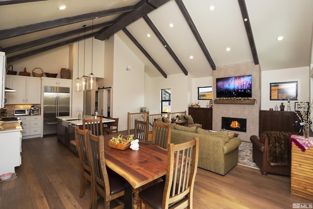 dining area with a barn door, dark wood-style flooring, a fireplace, high vaulted ceiling, and beam ceiling