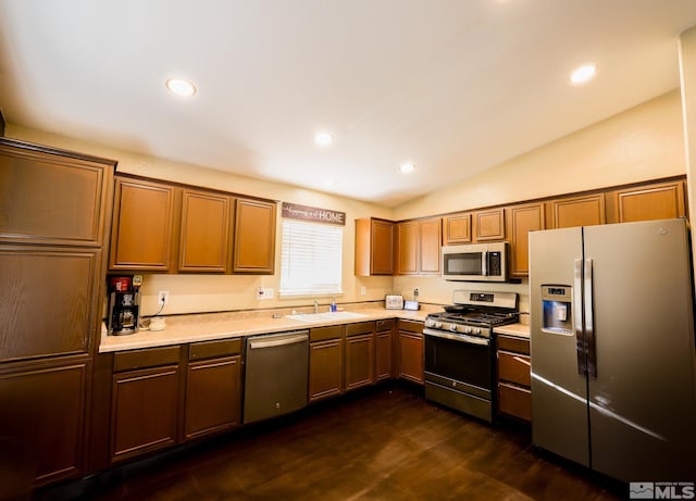 kitchen featuring lofted ceiling, a sink, light countertops, appliances with stainless steel finishes, and dark wood-style floors