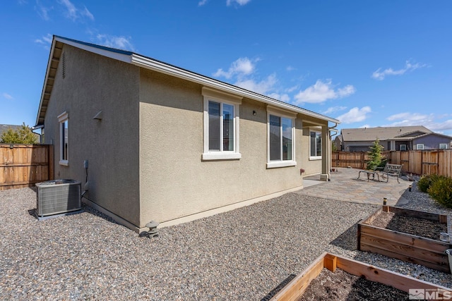 rear view of house featuring a vegetable garden, stucco siding, central AC unit, a patio area, and a fenced backyard