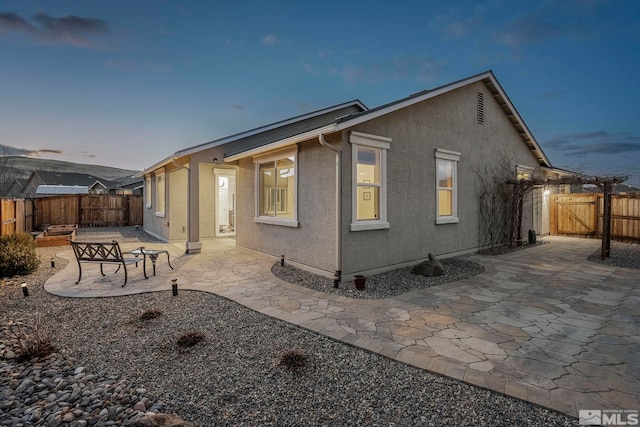 back of house at dusk with a patio area, fence, a gate, and stucco siding