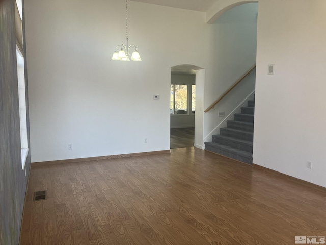 empty room with arched walkways, visible vents, stairway, wood finished floors, and baseboards