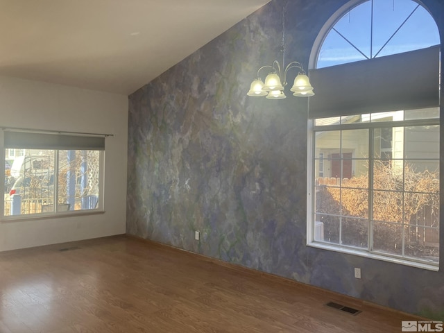 spare room with visible vents, a chandelier, vaulted ceiling, and wood finished floors