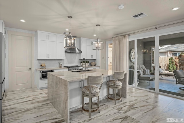 kitchen with light stone counters, visible vents, a sink, an island with sink, and wall chimney exhaust hood