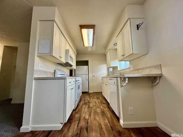 kitchen with white appliances, baseboards, white cabinets, a kitchen breakfast bar, and dark wood-type flooring