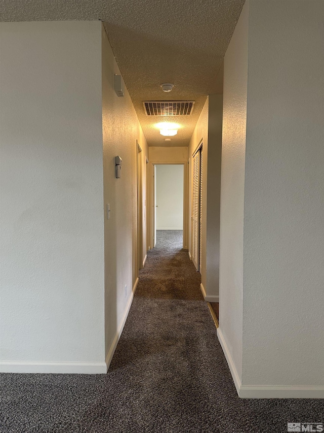 hallway featuring baseboards, visible vents, a textured wall, a textured ceiling, and carpet flooring