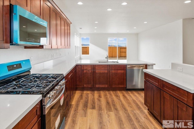 kitchen featuring stainless steel appliances, light countertops, light wood-style flooring, a sink, and a peninsula