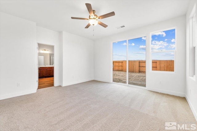 interior space featuring ensuite bathroom, light colored carpet, visible vents, baseboards, and access to outside