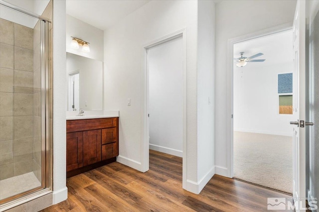 bathroom featuring ceiling fan, wood finished floors, vanity, baseboards, and a shower stall