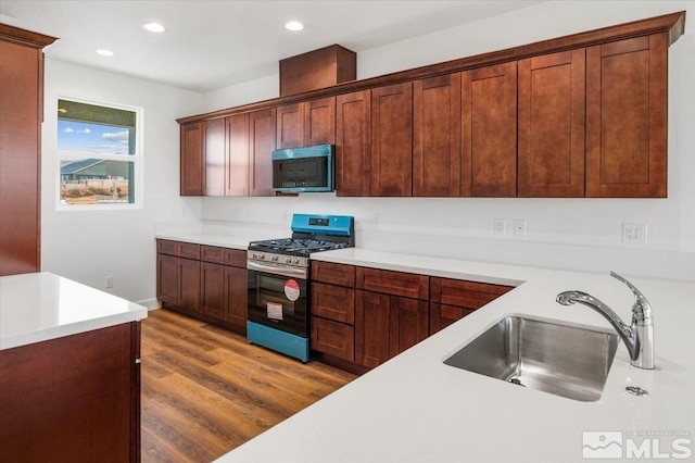 kitchen with recessed lighting, stainless steel appliances, wood finished floors, a sink, and light countertops