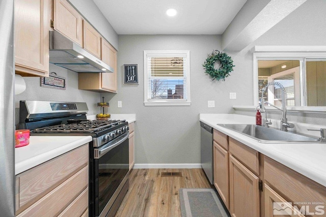 kitchen featuring under cabinet range hood, a sink, light wood-style floors, light countertops, and appliances with stainless steel finishes