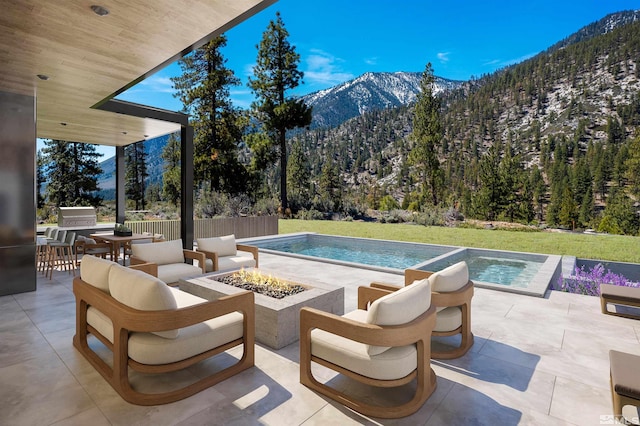 outdoor pool featuring an outdoor fire pit, a forest view, a yard, a patio area, and a mountain view