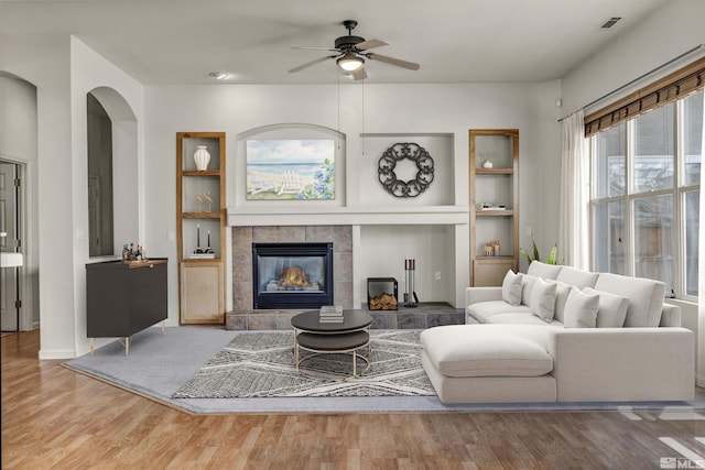 living room with built in shelves, wood finished floors, visible vents, ceiling fan, and a tile fireplace