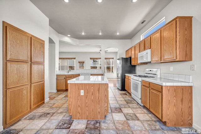 kitchen with white appliances, a kitchen island, a peninsula, recessed lighting, and tile counters