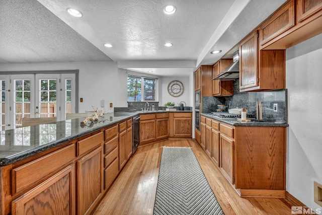 kitchen featuring stainless steel appliances, wall chimney exhaust hood, brown cabinetry, and light wood-style flooring