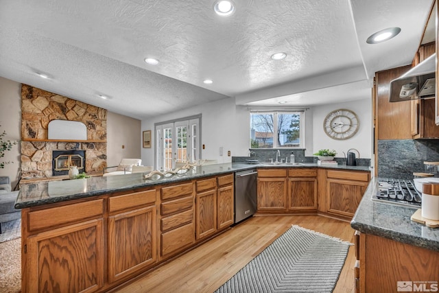 kitchen featuring brown cabinets, light wood-style flooring, dark stone counters, appliances with stainless steel finishes, and vaulted ceiling