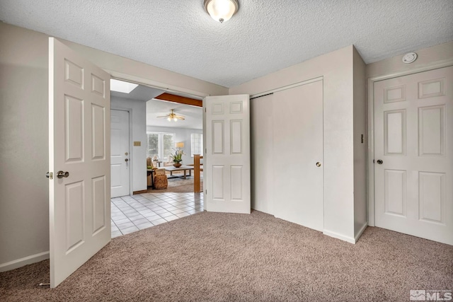 unfurnished bedroom featuring light tile patterned floors, light colored carpet, a closet, and a textured ceiling