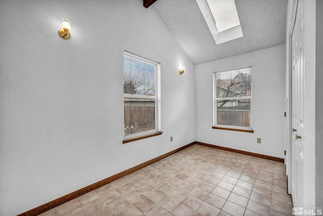 empty room featuring lofted ceiling with skylight, baseboards, a textured ceiling, and a wealth of natural light