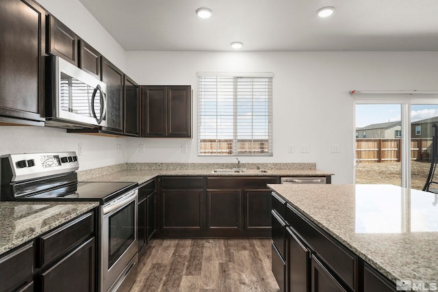 kitchen with a sink, light stone counters, recessed lighting, stainless steel appliances, and dark wood-style flooring