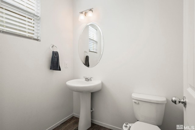 half bath with plenty of natural light, toilet, baseboards, and wood finished floors