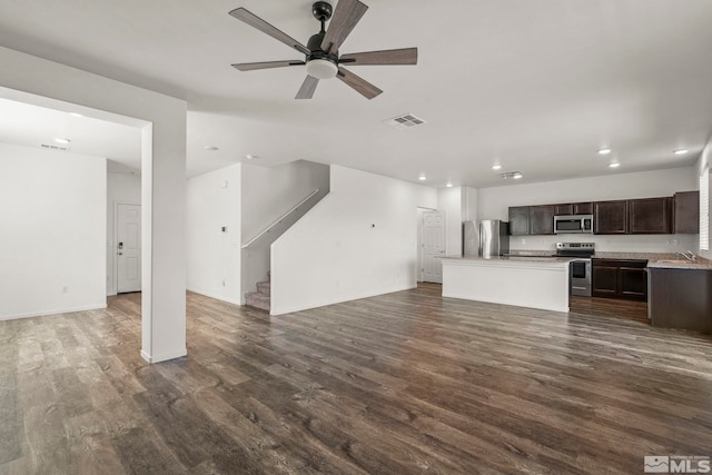 unfurnished living room with visible vents, a sink, stairs, ceiling fan, and dark wood-style flooring