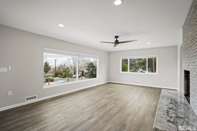 unfurnished living room featuring visible vents, a large fireplace, baseboards, and wood finished floors