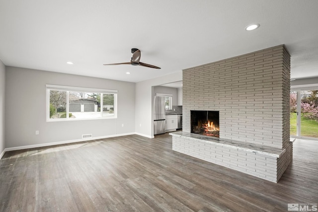 unfurnished living room featuring a ceiling fan, dark wood-style floors, visible vents, baseboards, and a fireplace