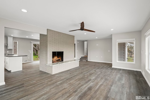 unfurnished living room featuring dark wood finished floors, a healthy amount of sunlight, a brick fireplace, and baseboards