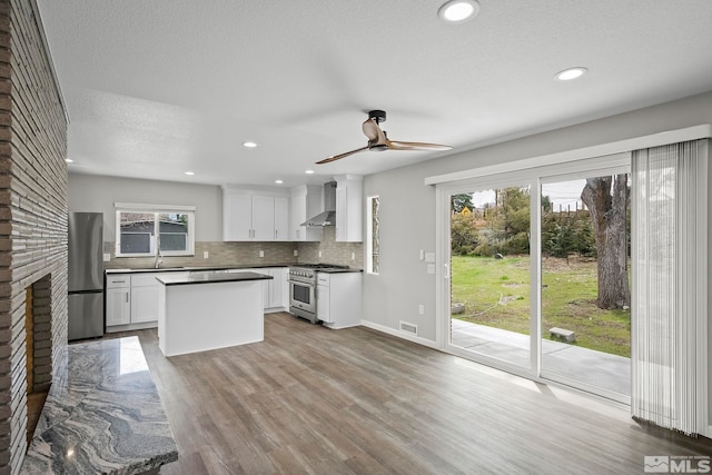 kitchen with a sink, stainless steel appliances, a healthy amount of sunlight, and wall chimney exhaust hood