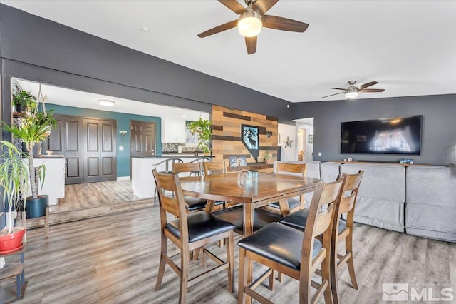 dining room with light wood-style flooring, an accent wall, and ceiling fan