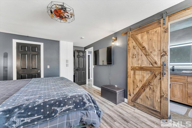 bedroom featuring a barn door, baseboards, and light wood-type flooring