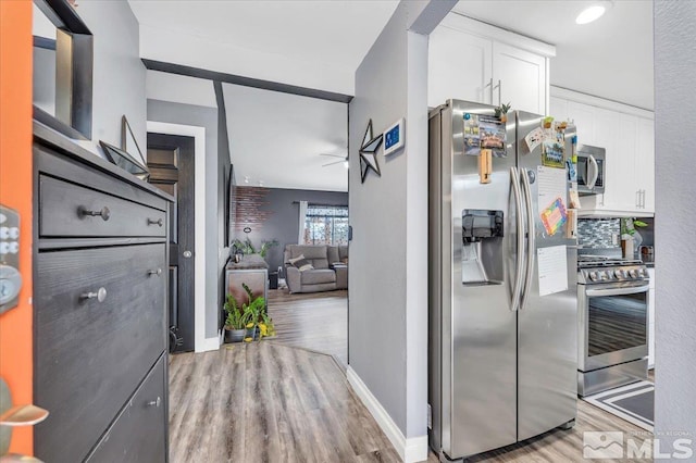 kitchen featuring light wood-style flooring, tasteful backsplash, stainless steel appliances, white cabinets, and baseboards