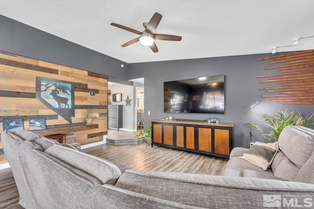 living area featuring wood finished floors, wooden walls, baseboards, ceiling fan, and an accent wall