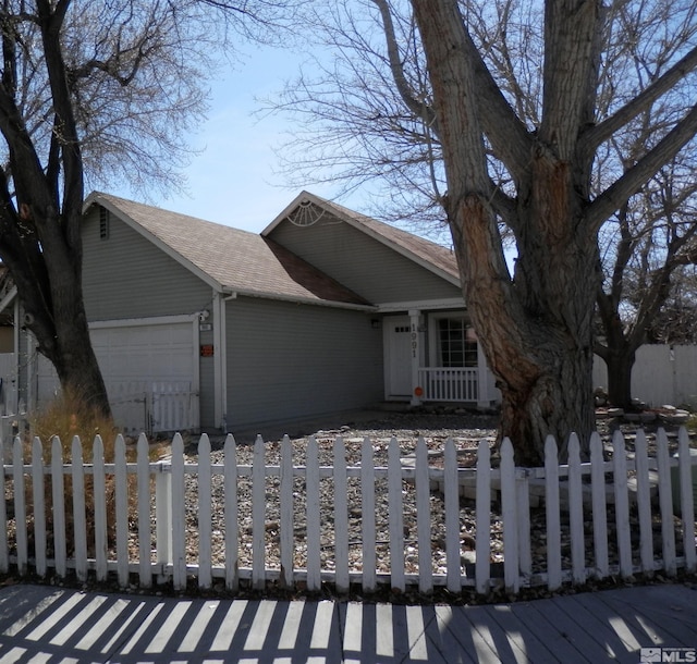 view of front of home with an attached garage, a fenced front yard, and a shingled roof