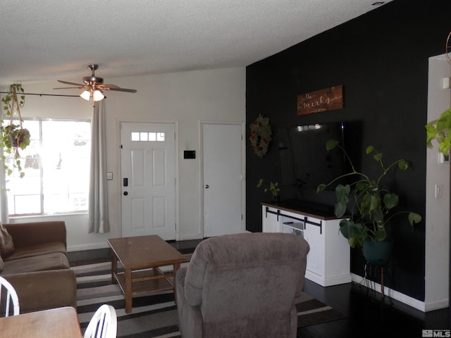 living area featuring a ceiling fan, dark wood-style floors, baseboards, lofted ceiling, and a textured ceiling