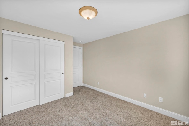 unfurnished bedroom with a closet, light colored carpet, and baseboards