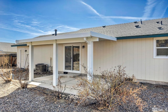 back of property with fence, roof with shingles, central AC unit, and a patio area