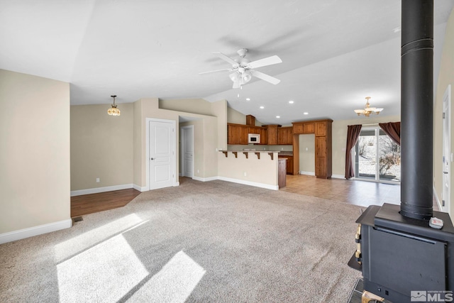 unfurnished living room featuring light carpet, lofted ceiling, a ceiling fan, baseboards, and a wood stove