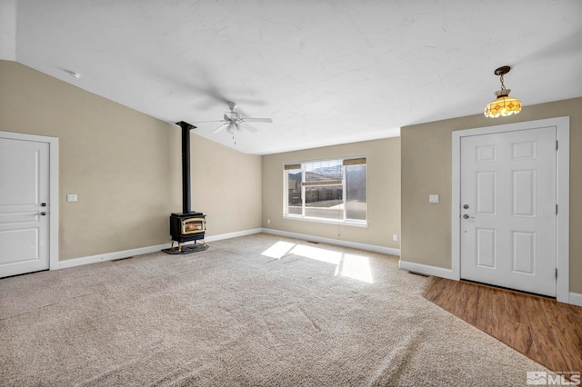 unfurnished living room featuring baseboards, carpet floors, a wood stove, and vaulted ceiling